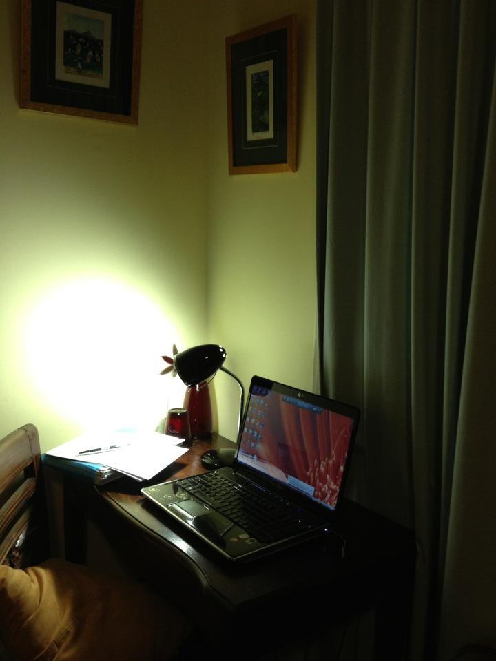 Small desk set up with laptop, reading lamp and notes